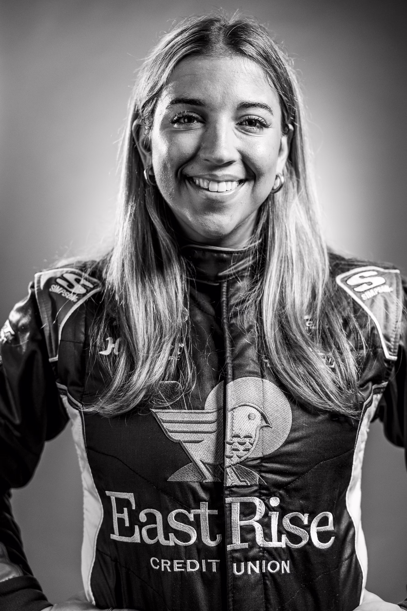 Taylor Hoar standing, smiling at the camera while wearing the EastRise racing suit