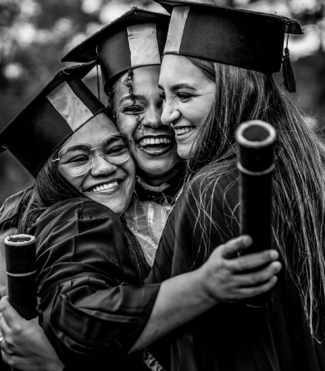 Three college graduates embracing.