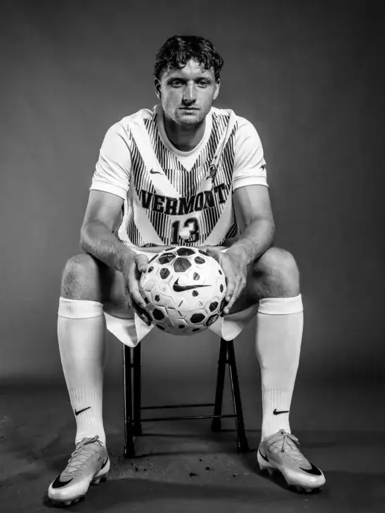 David Ismail sitting in a chair, holding a soccer ball in his hands while leaning forward with his elbows on his knees looking at the camera.
