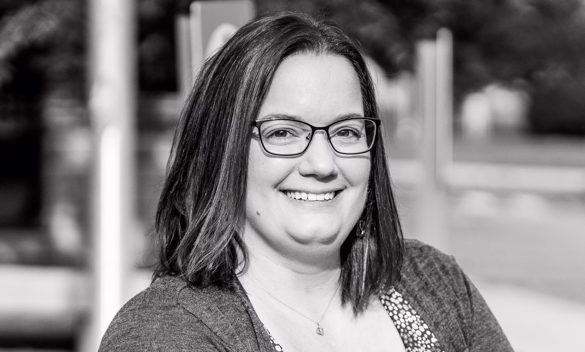 Waterbury branch manager Morgan Pratt looking into the camera while smiling standing outside, wearing glasses and a flowered shirt with a cardigan over it.