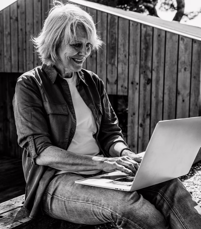 Older woman on a laptop sitting outside.