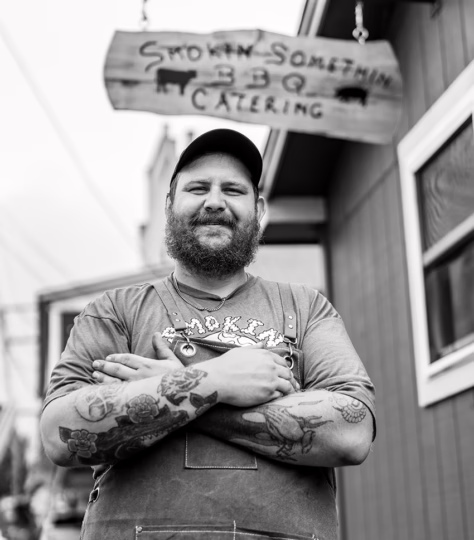 Smiling man standing outside of barbeque restaurant with his arms crossed.