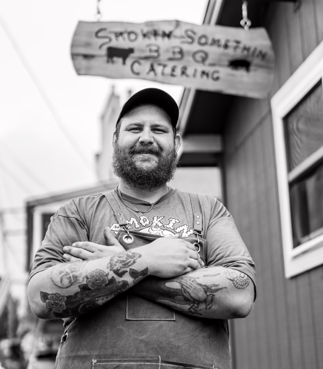 Smiling man standing outside of barbeque restaurant with his arms crossed.