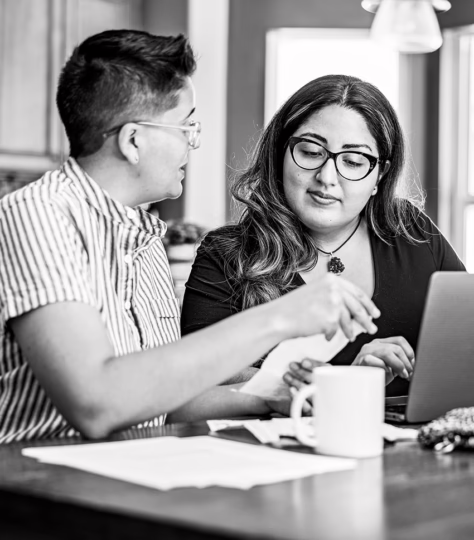 Two partners at a table looking at a laptop with a cup of coffee discussing finances