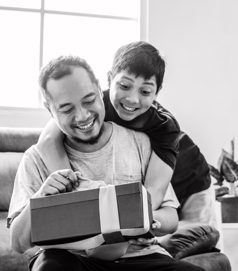 A son watches as his father opens up a holiday gift with a ribbon.