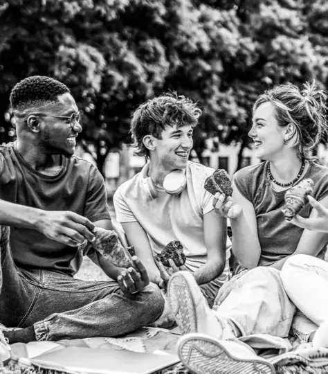 Three friends eating pastries together in a park.