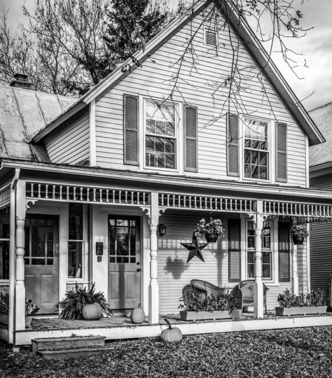 House in the fall with fall flowers and a star hanging on the front porch. New England style home, a tree in front of it with no leaves.