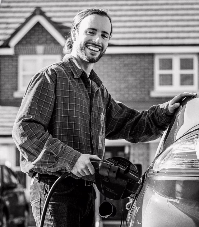 Man charging electric vehicle and smiling