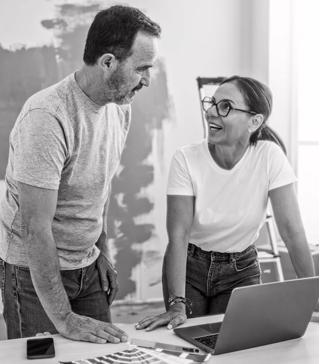 Man and woman discuss financial decisions while hovered over a laptop and paint swatches.