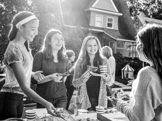 Teens standing at a table smiling outside eating pizza