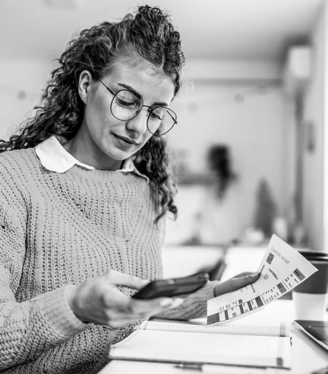 Woman with a document in left hand while looking at her phone in her right hand
