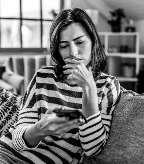 Concerned woman sitting on a couch looking at her phone.